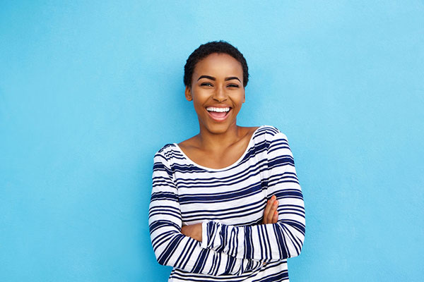 young woman in striped shirt smiling with her new porcelain veneers in front of a blue background